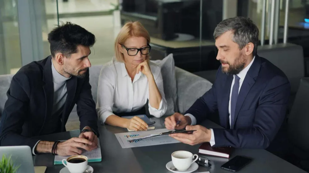 Two business owners reviewing financial charts with an advisor across a conference table