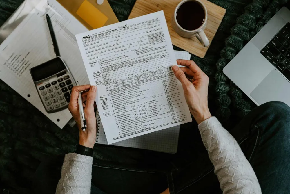 Overhead view of a person reviewing a Form 1040 tax return with a calculator and coffee
